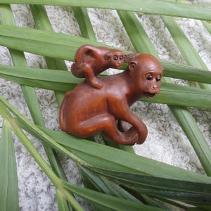 May include: A wooden carving of two monkeys, one riding on the back of the other. The monkeys are brown and have black eyes. The carving is detailed and realistic.