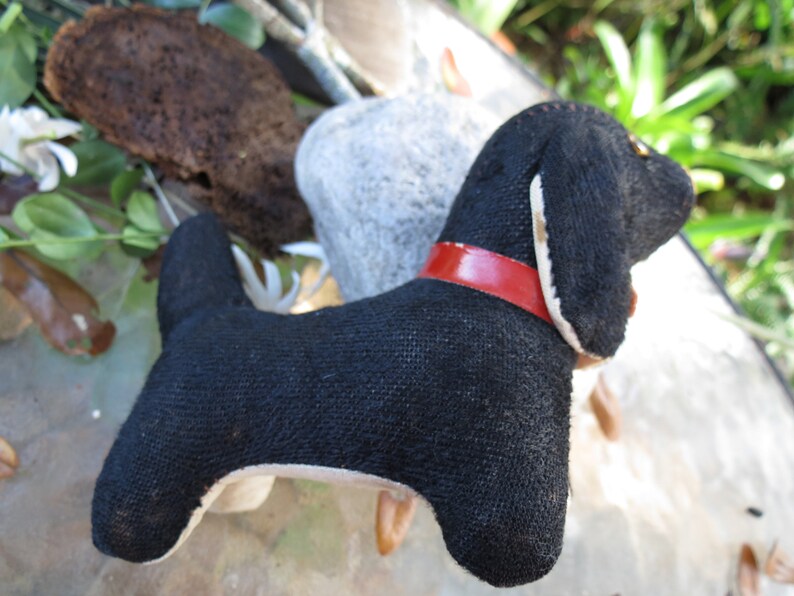 May include: A handmade black dog plush toy with a red collar. The dog has a long body and floppy ears. The toy is made of a textured fabric and has white accents on the ears and belly. The dog is a charming decorative item.