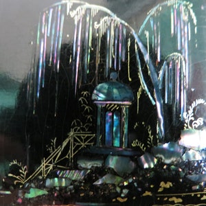 Pu&ograve; includere: Una scatola laccata nera con un design decorativo di un pagoda e alberi realizzati in madreperla iridescente. Il design &egrave; su uno sfondo nero.