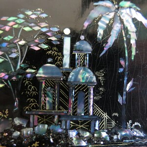 Pu&ograve; includere: Una scatola laccata nera con una scena decorativa di una palma e due strutture simili a pagode realizzate in madreperla iridescente. La scena &egrave; su uno sfondo nero con accenti dorati.
