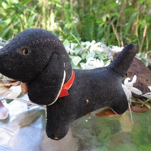 May include: A vintage black stuffed dog with a red collar. The dog has floppy ears, a stitched nose, and a small tail. The toy is made of a textured fabric and has a charming, aged appearance. A classic collectible.