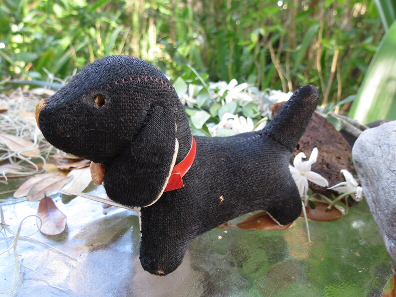 May include: A vintage black stuffed dog with a red collar. The dog has floppy ears, a stitched nose, and a small tail. The toy is made of a textured fabric and has a charming, aged appearance. A classic collectible.