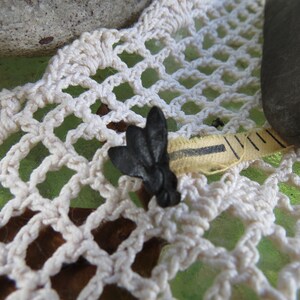 Pu&ograve; includere: Un metro a nastro nero e giallo con un tappo a forma di farfalla nero. Il nastro &egrave; appoggiato su un pizzo bianco all'uncinetto.