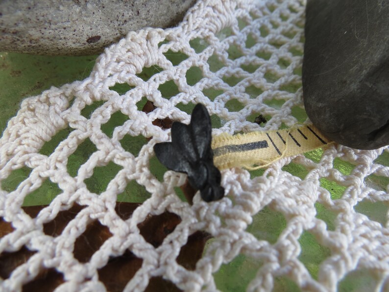 Pu&ograve; includere: Un metro a nastro nero e giallo con un tappo a forma di farfalla nero. Il nastro &egrave; appoggiato su un pizzo bianco all'uncinetto.