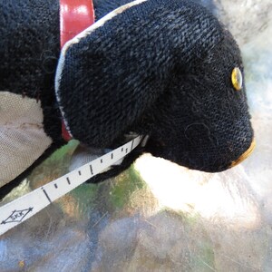May include: A black stuffed dog with a red collar and a white and black measuring tape. The dog has a yellow eye and a tan nose. The measuring tape is marked in inches and has the word "JAPAN" printed on it.