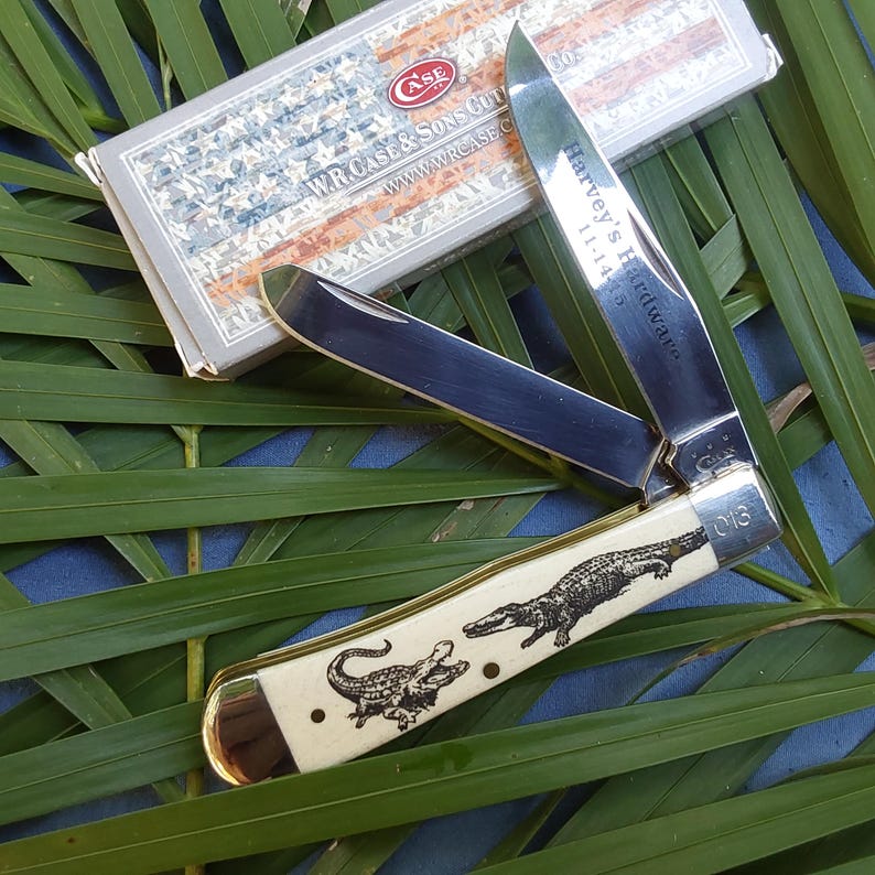 May include: A Case XX pocket knife with a white bone handle featuring an alligator design. The blade is open and the knife is engraved with "Harvey's Hardware 11-1-14".