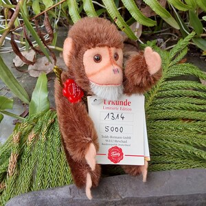 May include: A brown plush monkey with a light peach face, ears, and hands. The monkey has a white beard and a red wax seal. A tag reads "Urkunde Limitierte Edition" and the numbers "1314" and "5000".