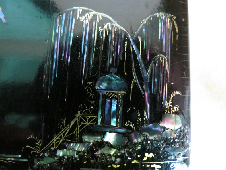 Pu&ograve; includere: Una scatola laccata nera con una scena di un pagoda e alberi intarsiati con madreperla iridescente. La scena &egrave; delineata con vernice dorata.