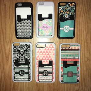 May include: Six different phone cases with a built-in card holder. The cases are white with various patterns and designs, including geometric shapes, floral patterns, and a black and white damask design. Each case has a personalized name or initial on the card holder.