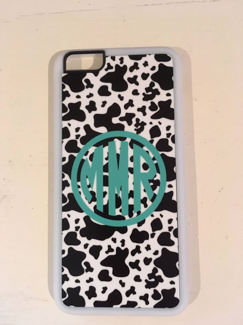 May include: A white phone case with a black and white cow print design. The case has a teal monogram in a circle that says "MMR".