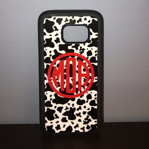 May include: A black phone case with a white and black cow print design. A red circle with the letters "MOA" in white is centered on the case.