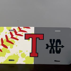 May include: A gray and white personalized license plate with a softball design on the left side and the letter "T" in red on the right side. The right side also has a black and white graphic of a cross arrow with the letters "XC" in the center.