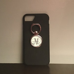 May include: Black phone case with a silver ring holder and a white volleyball with the letter "M" on it.