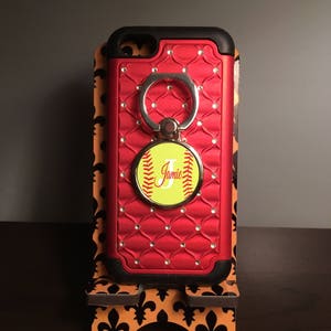 May include: Red phone case with a diamond pattern and a ring holder. The ring holder has a softball with the letter "J" and the name "Jamie" on it.