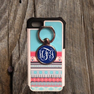 May include: A white phone case with a blue, pink, and gray geometric pattern. The case has a silver ring holder with a blue circle monogrammed with the letters "H.F.J."