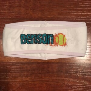 May include: White headband with a teal and black graphic of the word "Benson" and a yellow softball with orange flames.