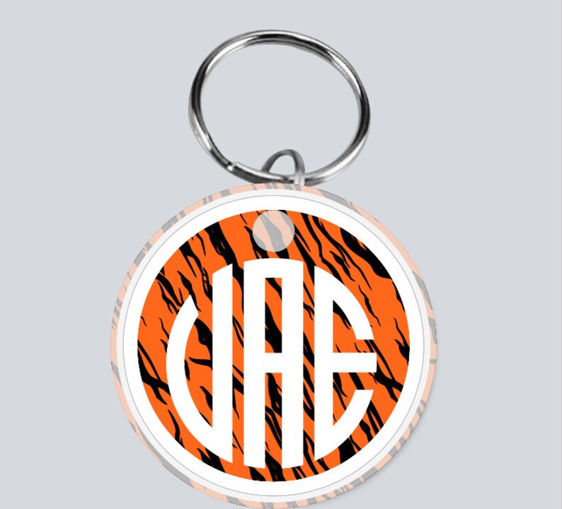 May include: A round orange and black tiger print keychain with a white circle in the center. The white circle has the letters "VAE" in black.