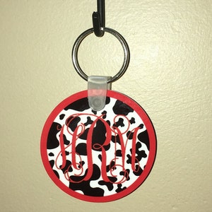May include: A black and white cow print keychain with a red border and a red monogram "RM" in the center.