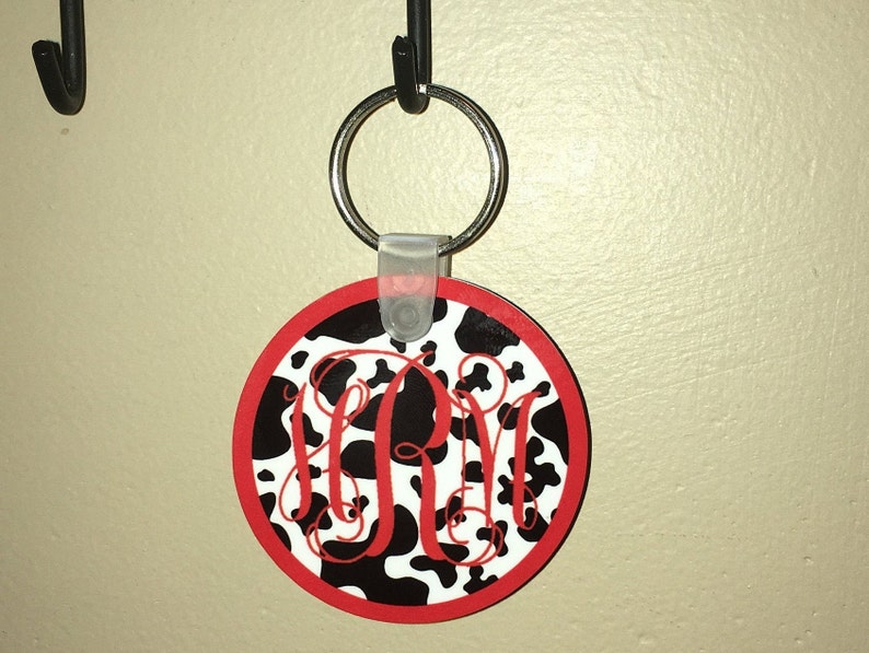May include: A black and white cow print keychain with a red border and a red monogram "RM" in the center.