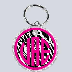 May include: A round keychain with a black and white zebra print background. The keychain has a pink circle with the letters "VAE" in white inside the circle.
