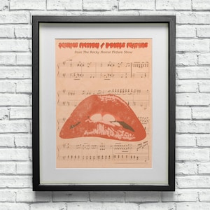 May include: A framed print of sheet music with the title "Science Fiction/Double Feature" from the movie "The Rocky Horror Picture Show". The music is overlaid with a red and black image of a pair of lips.