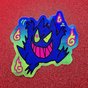 Könnte beinhalten: Blauer Aufkleber mit einem Cartoon-Geist mit breitem rosa Grinsen, grünen Augen und rosa und grünen Flammen. Der Aufkleber hat eine neon-grüne und blaue Kontur, vor rotem Hintergrund.