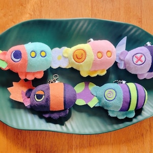 May include: Five colorful plush toys shaped like submarines with different designs and colors. The toys are on a green leaf-shaped plate.
