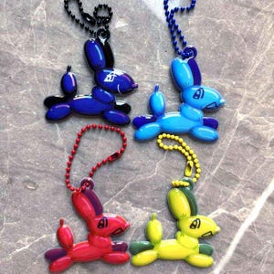 May include: Four balloon animal keychains in the shape of rabbits. The keychains are blue, light blue, red, and yellow. Each keychain has a metal chain attached to it.