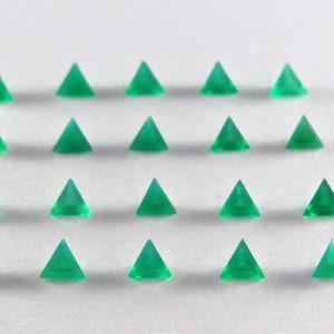 Könnte beinhalten: Eine Sammlung von 18 grünen dreieckigen Edelsteinen, die in Reihen auf einer weißen Oberfläche angeordnet sind.
