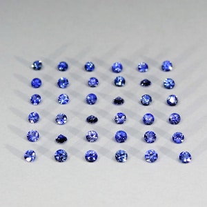 May include: A collection of thirty-six round, faceted blue gemstones arranged in a six-by-six grid pattern. Each individual stone displays a brilliant cut with multiple facets that reflect light, creating a uniform appearance across the set.