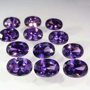 May include: Ten oval-shaped, purple gemstones. The gemstones are faceted and have a shiny, polished finish.