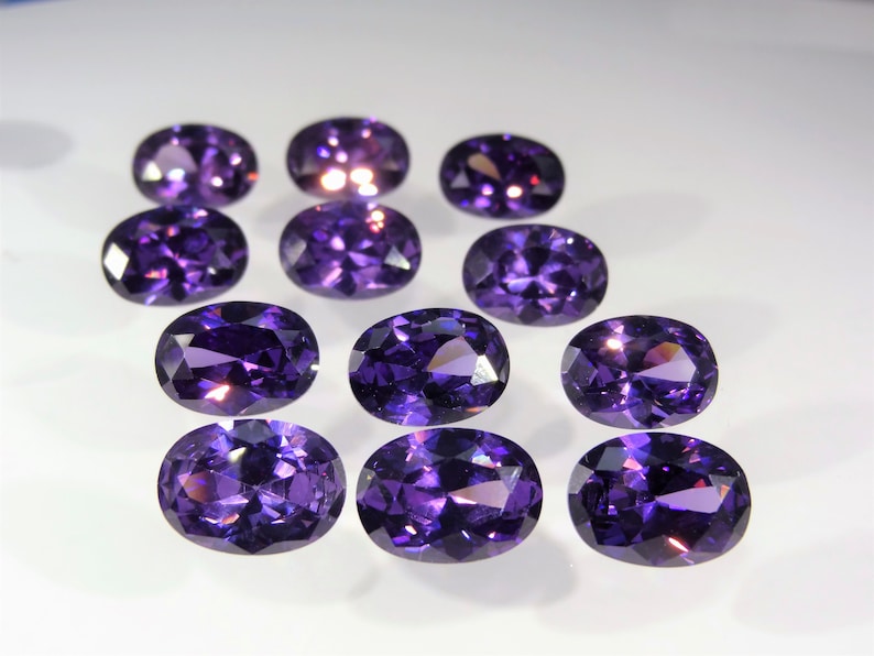 May include: Ten oval-shaped, purple gemstones. The gemstones are faceted and have a shiny, polished finish.