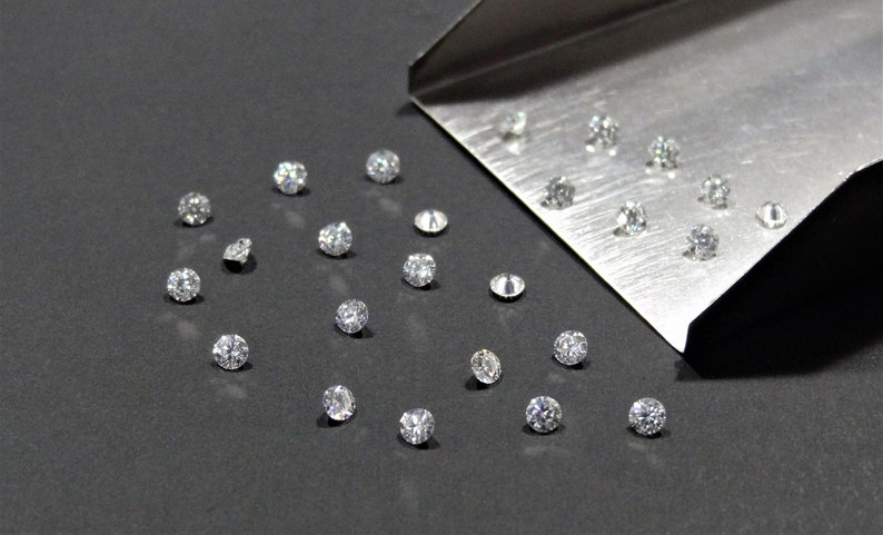 May include: A collection of loose diamonds on a black surface, with some diamonds spilling out of a metal tray.
