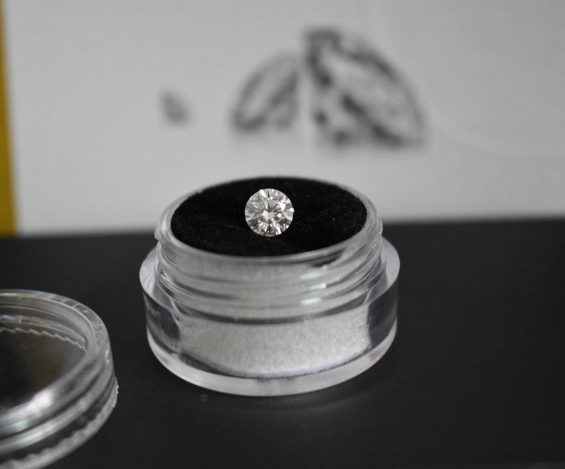 May include: A clear plastic container with a black velvet interior holds a round, clear diamond.