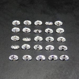 Peut inclure: Une collection de 20 pierres précieuses ovales transparentes disposées en grille sur une surface noire.