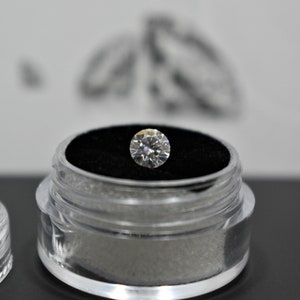 May include: A clear plastic container with a black velvet interior holds a round, clear diamond.