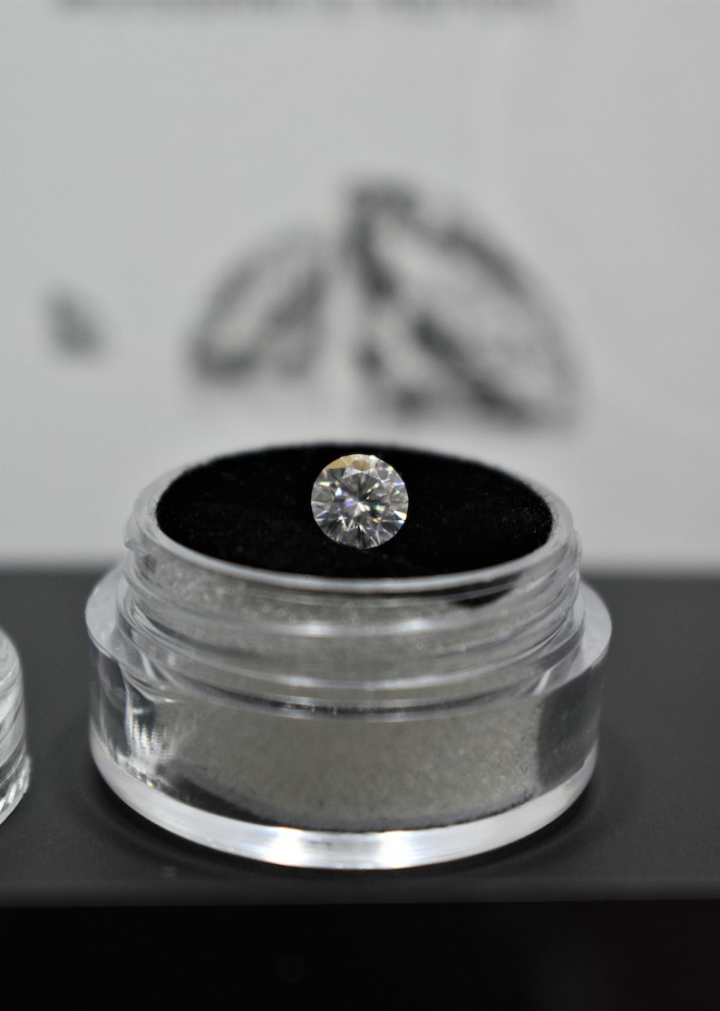 May include: A clear plastic container with a black velvet interior holds a round, clear diamond.