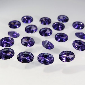 May include: A collection of 17 oval-shaped purple gemstones, likely amethyst, displayed on a white surface.