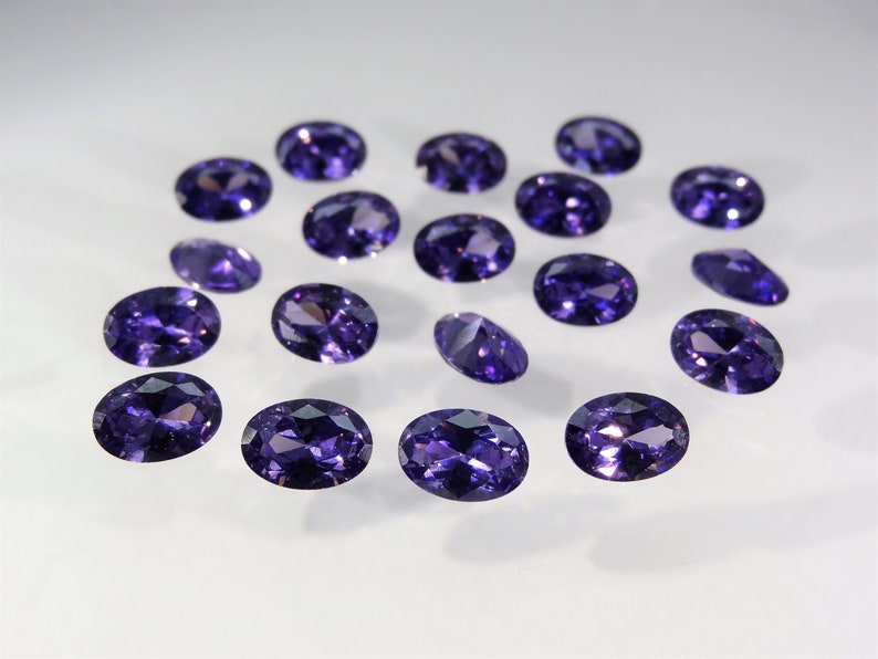 May include: A collection of 17 oval-shaped purple gemstones, likely amethyst, displayed on a white surface.