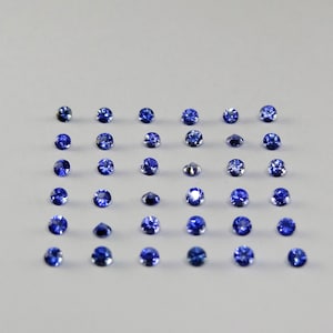 May include: A collection of thirty-six small, round, faceted blue gemstones arranged in a six-by-six grid. Each stone displays a deep, vibrant blue hue with reflective surfaces that catch the light, showcasing a uniform circular cut and polished finish.