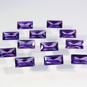 May include: A collection of twelve rectangular, faceted purple gemstones arranged in a loose cluster. Each stone features a clear, deep violet hue with sharp, geometric edges and a polished surface that reflects light across its multiple facets.