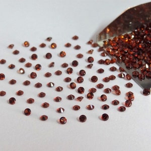 Può includere: Una piccola paletta di metallo piena di pietre preziose rosse sciolte, con alcune che si riversano su una superficie bianca.