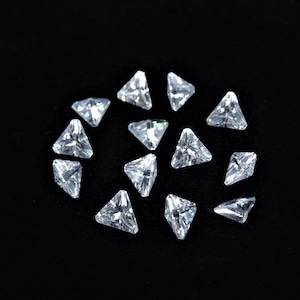 Puede incluir: Un grupo de 15 piedras de cristal triangulares transparentes sobre un fondo negro.