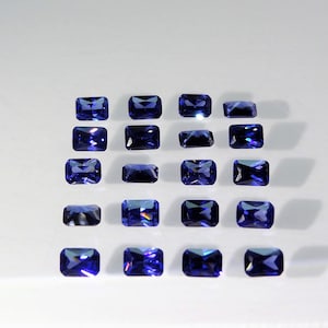 Op de afbeelding: Een verzameling van twintig rechthoekige, gefacetteerde blauwe edelstenen gerangschikt in een rasterpatroon. Elke steen heeft een diepe, levendige blauwe kleur met meerdere facetten die het licht reflecteren voor een sprankelend uiterlijk.
