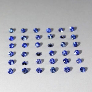 May include: A collection of thirty small, round, faceted blue gemstones arranged in a grid of six rows and five columns. Each gemstone displays a brilliant cut with multiple reflective surfaces, showcasing a deep, vibrant blue color throughout.