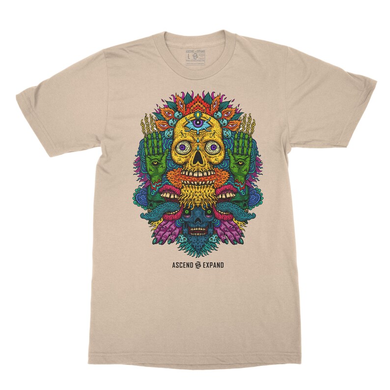 May include: A beige t-shirt with a colorful graphic print of a skull with a third eye, surrounded by hands and mouths. The text "ASCEND & EXPAND" is printed below the graphic.