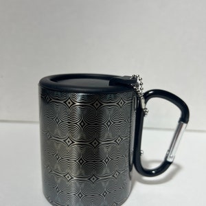 May include: A black and silver travel mug with a geometric pattern and a black carabiner handle.