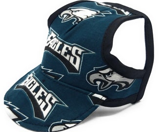 May include: A teal blue dog hat with a black adjustable strap. The hat has a white and black Philadelphia Eagles logo repeated on the fabric.