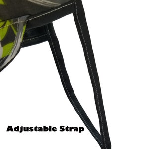 May include: Close-up of a black adjustable strap with a white plastic buckle. The strap is attached to a green and black patterned fabric.