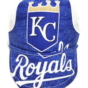 May include: A blue and white cycling cap with a white "Royals" logo and a gold crown above the letters "KC".
